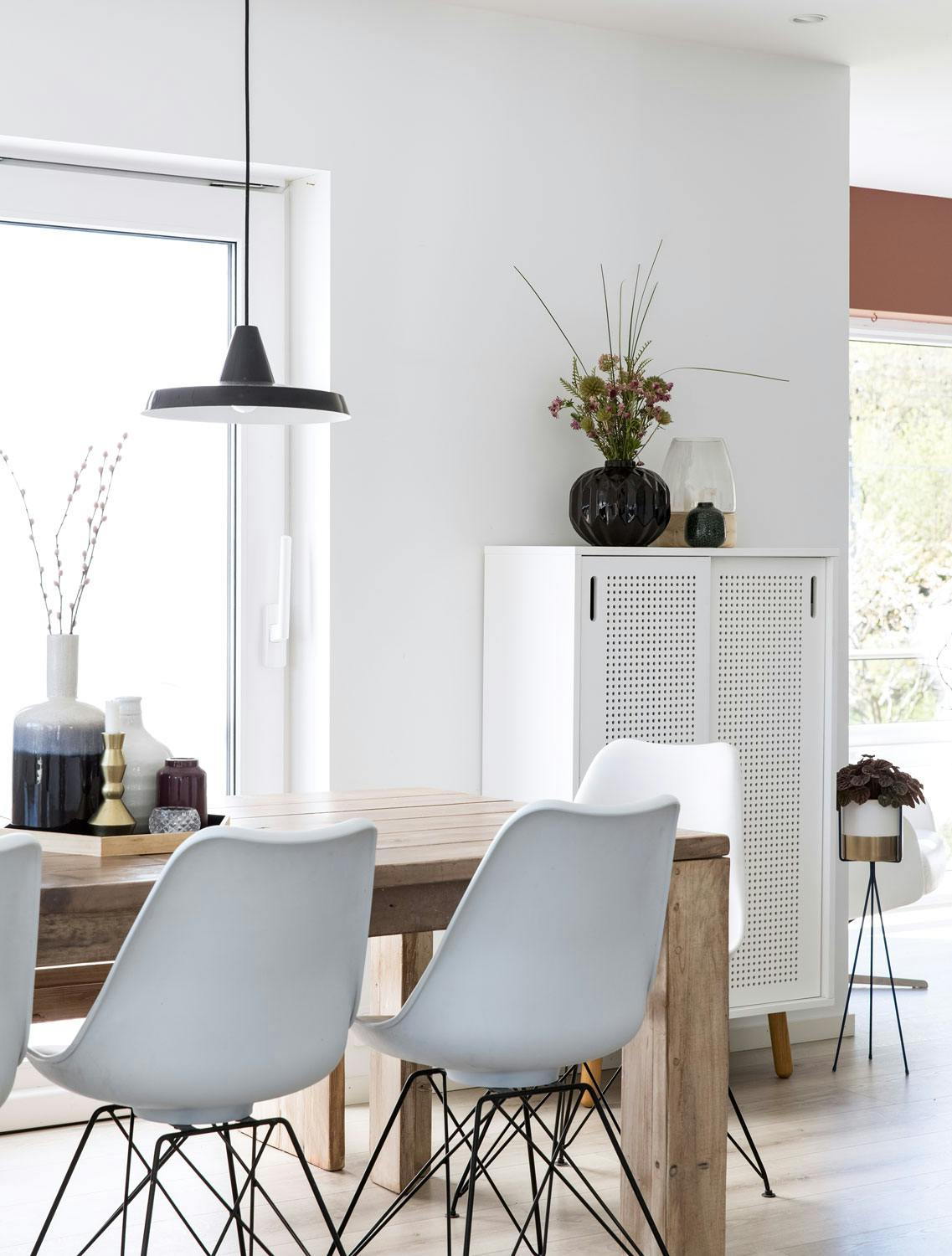 Lys og kontraster i fin balanse i spisestuen Lys spisestue i en nordisk stil med massivt rustikt trebord og hvite Eames-stoler